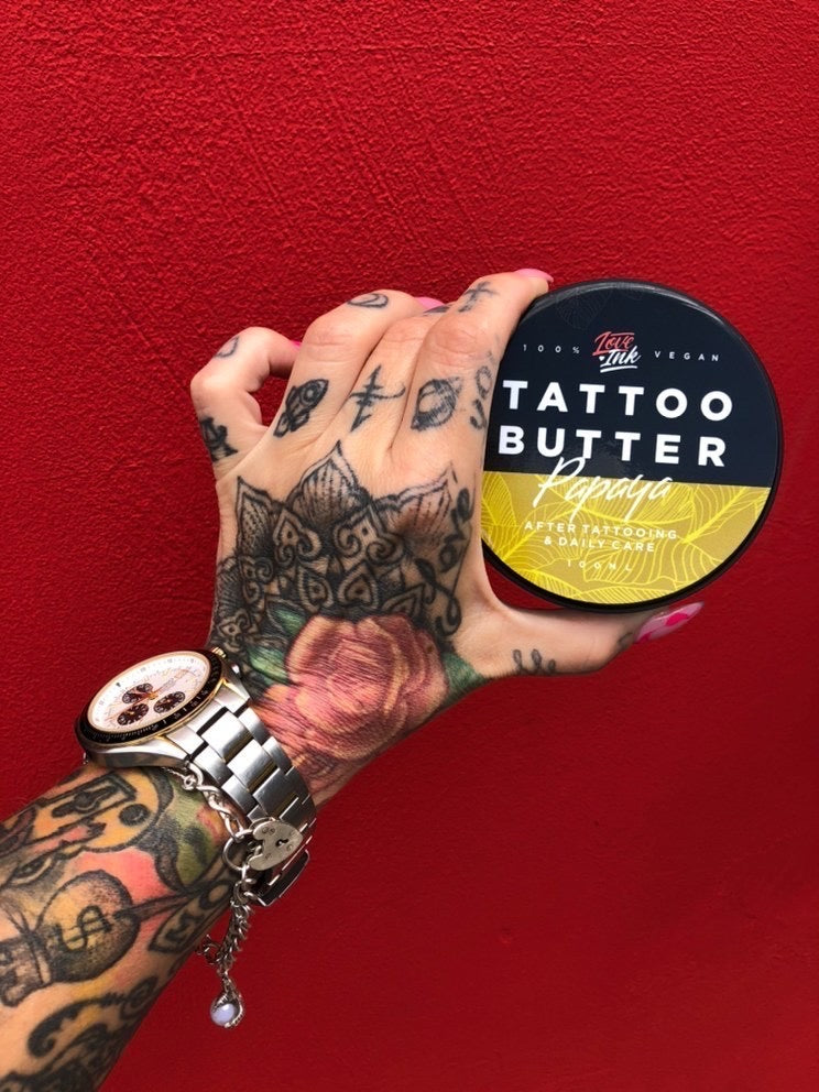 Hand holding a jar of Tattoo Butter Papaya by LoveInk against a vibrant red background, emphasizing the product's packaging and design.