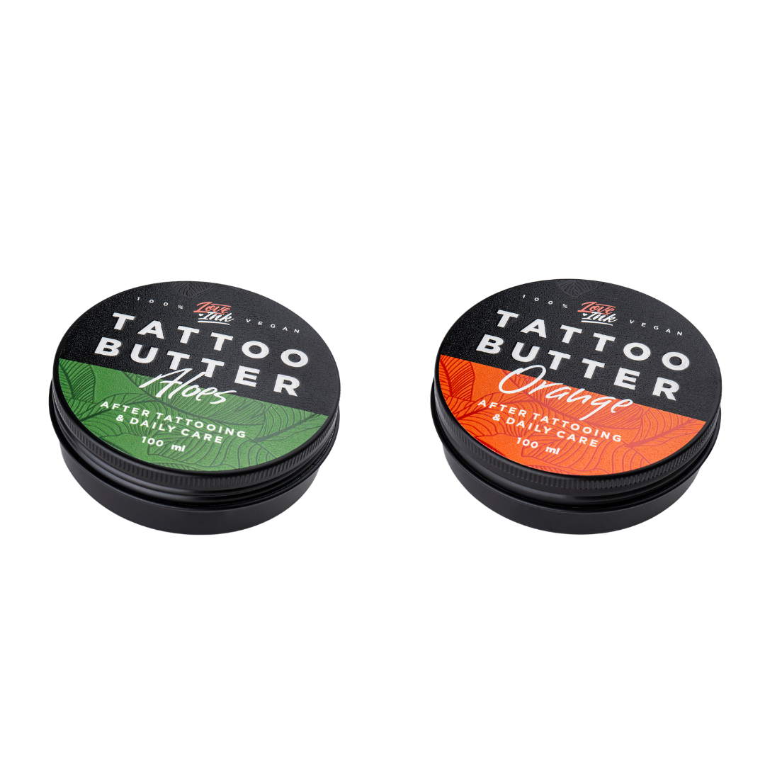 Two tins of Love Ink Tattoo Butter on a transparent background. One tin is labeled 'Aloe' with a green design, and the other is labeled 'Orange' with an orange design. Both tins are 100 ml and are intended for after tattooing and daily care.