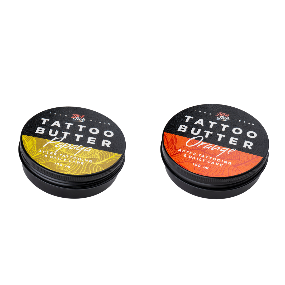 Two tins of Love Ink Tattoo Butter on a transparent background. One tin is labeled 'Orange' with an orange design, and the other is labeled 'Papaya' with an yellow design. Both tins are 100 ml and are intended for after tattooing and daily care.