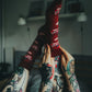 Tattooed legs raised with feet wearing red socks featuring a cartoon cat with a unicorn horn (Kotorozec) and hearts, set in a cozy indoor setting.