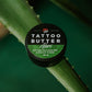 Tin of Love Ink Tattoo Butter Aloe, 50 ml, placed on an aloe leaf, with a green background.