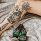 Tattooed legs on a bed with Love Ink Tattoo Butter Aloe and Tattoo Oil Aloe bottles next to them.